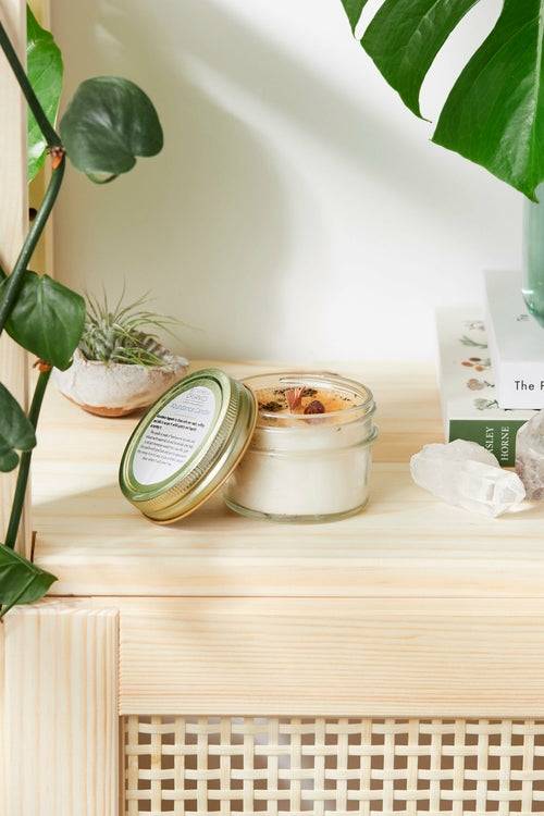 Hand-poured 4 oz Abundance Candle in glass jar with metal lid, infused with organic essential oils, topped with herbs and citrine crystal for wealth and blessings.